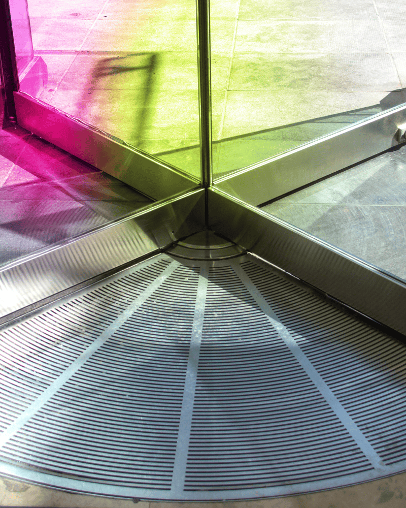 Glass revolving door, tinted with shades of purple and lime green that represent acre's brand colors