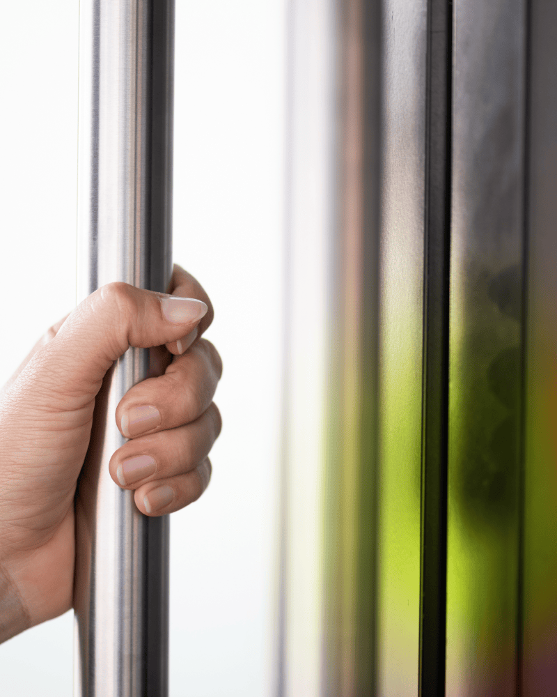 Close up of a hand gripping a vertical metal door handle